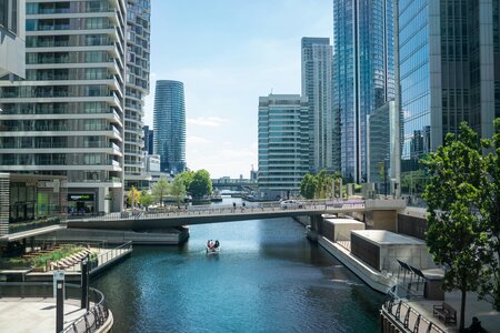 A cityscape shot of London with a bridge passing horizontally over a river through the middle, and glass skyscrapers lined with trees on the side.